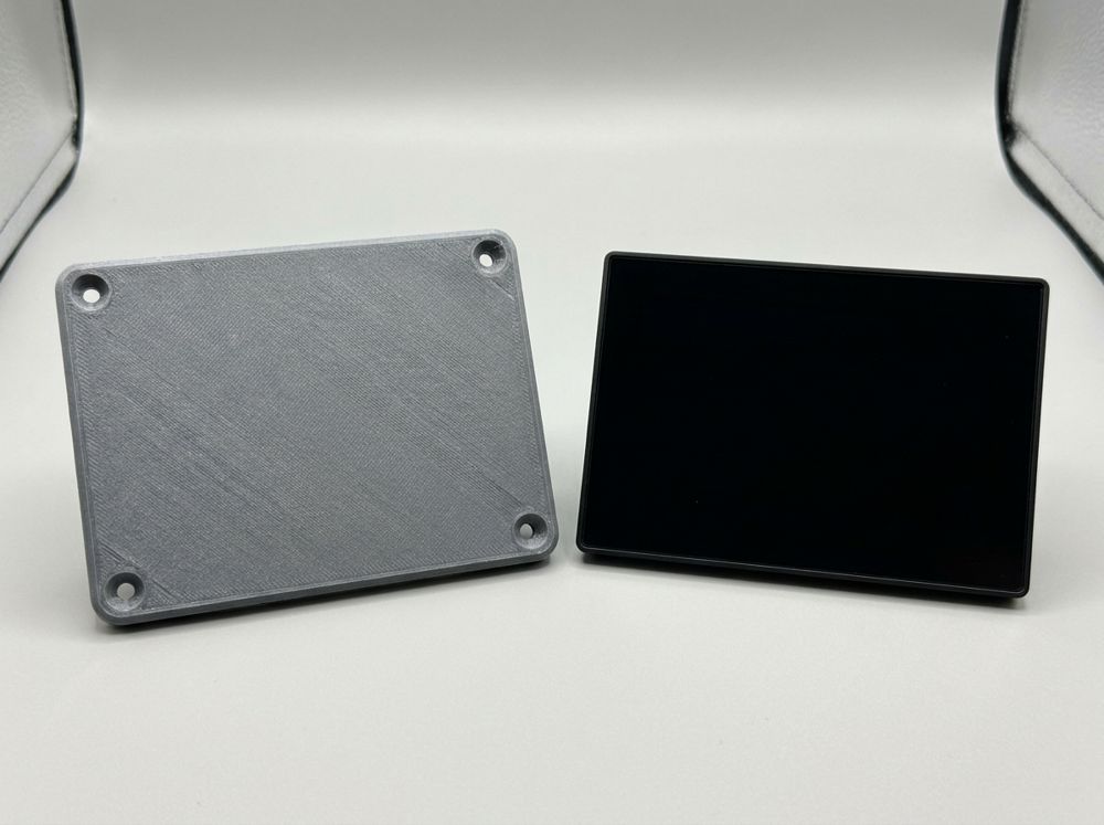 Concept render of a gray adapter plate with four screw holes beside a black display